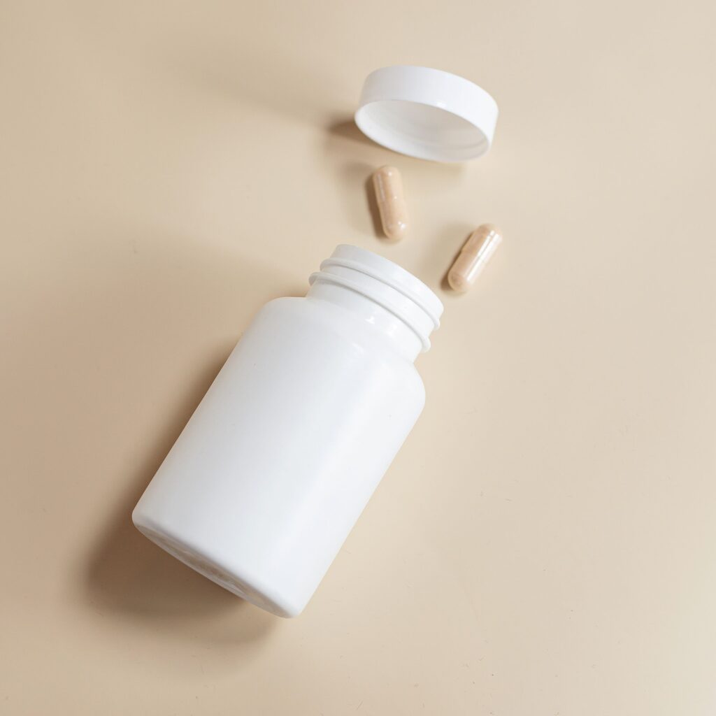 White pill bottle with capsules spilled on a beige surface